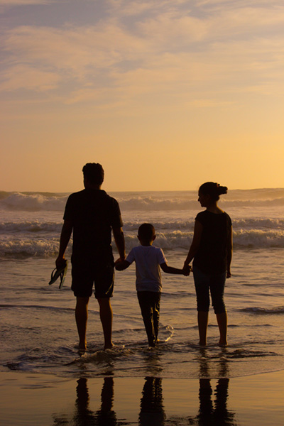 A father, son and wife holding hands on a beach